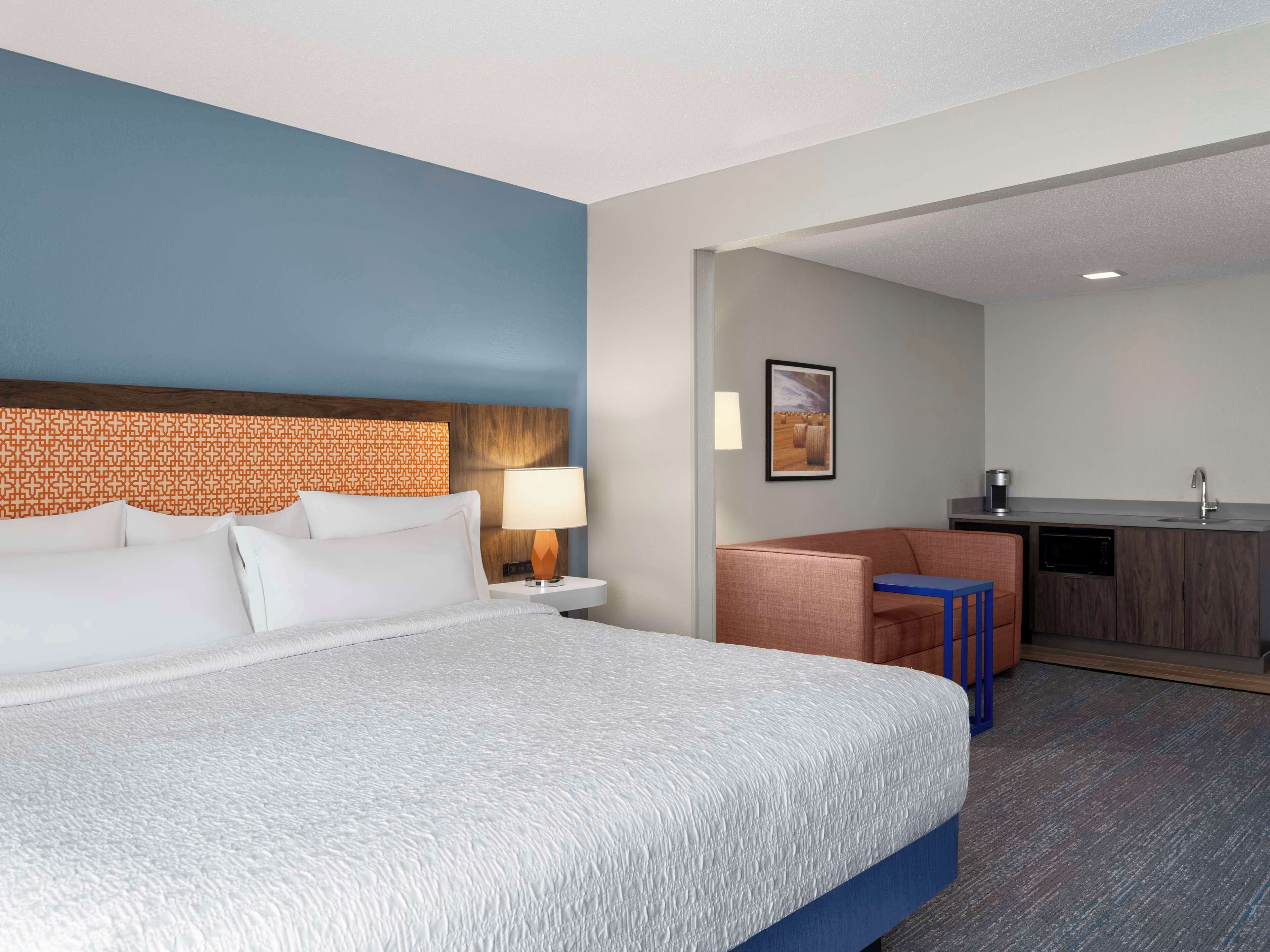A hotel room with a bed, a desk, a chair, a lamp, and a picture on the wall.