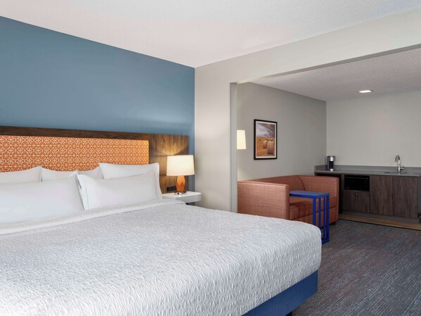 A hotel room with a bed, a desk, a chair, a lamp, and a picture on the wall.