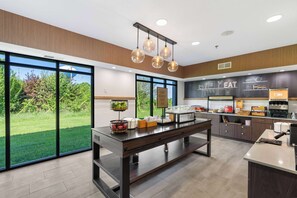 A modern kitchen with large windows, a buffet counter, and a chalkboard menu.