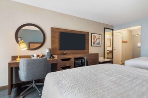 A hotel room with a desk, a chair, a television, a microwave, and two beds.