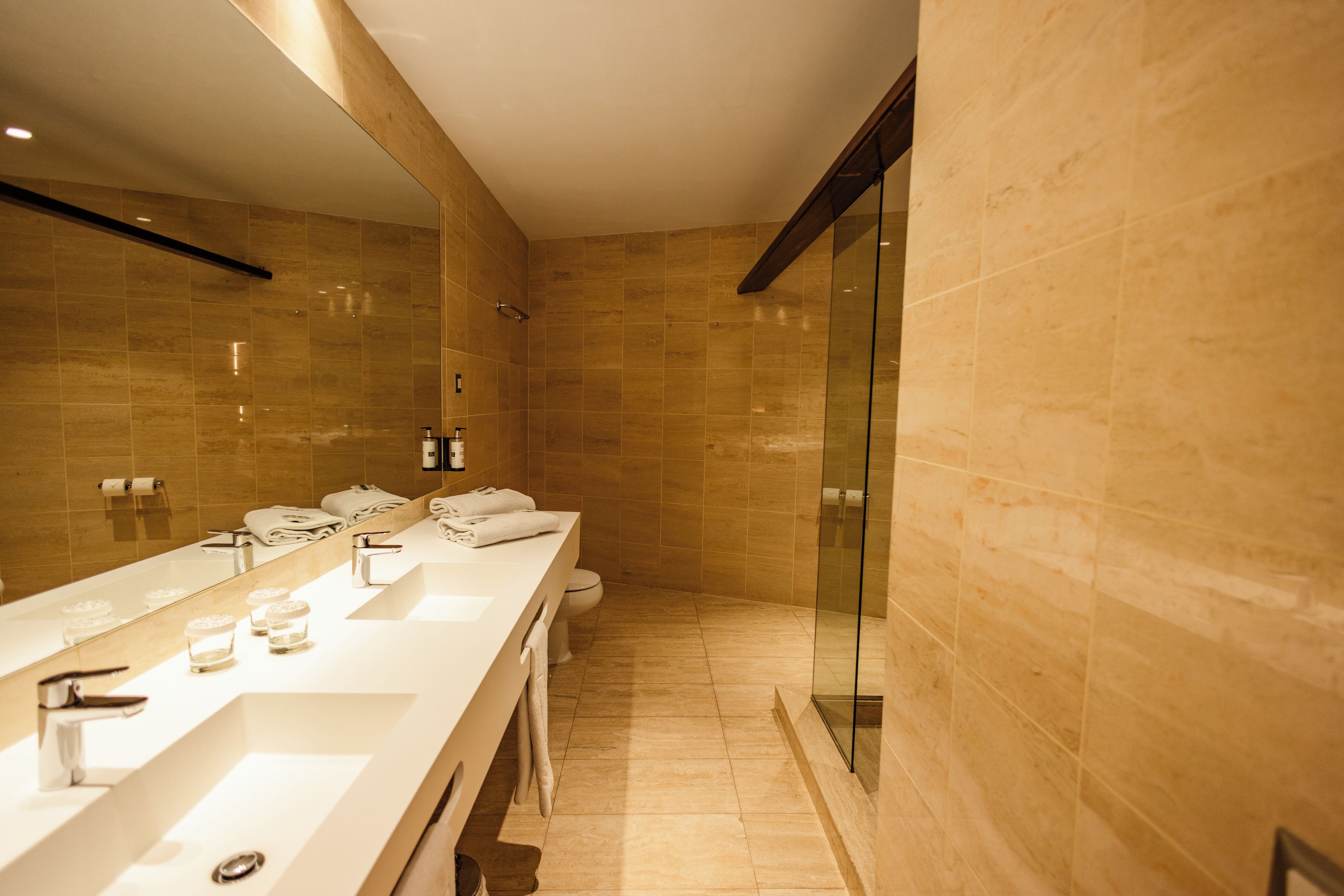 A modern bathroom with a long vanity, a glass shower enclosure, and a large mirror.