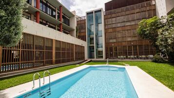 A swimming pool with a metal ladder, surrounded by a well-maintained lawn and modern buildings with large windows and balconies.