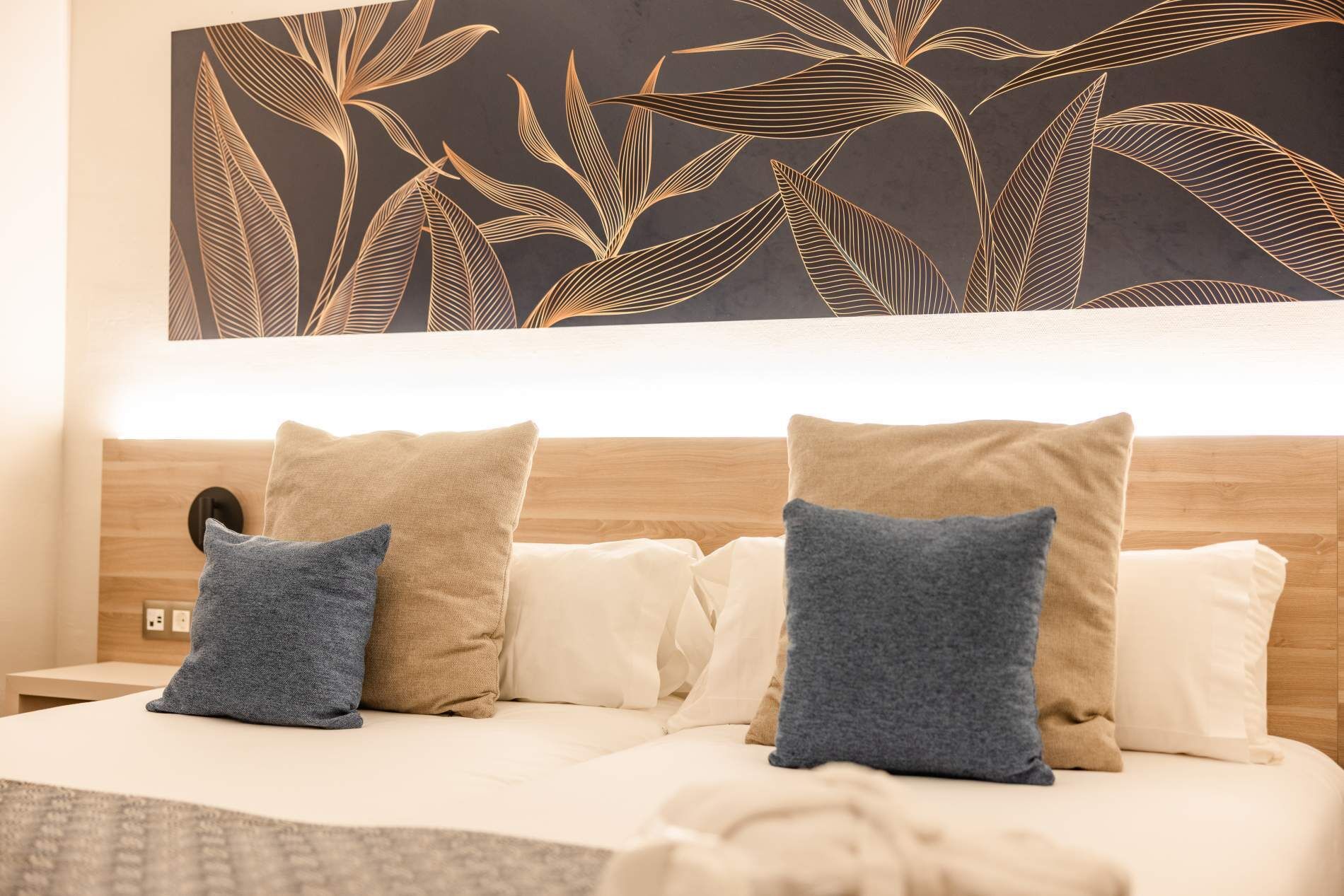 Un letto con due cuscini, una parete decorata con un motivo a foglia e una testiera in legno.