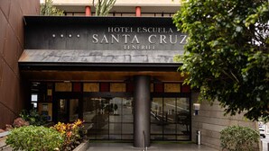 L’entrée de l’hôtel-école Santa Cruz, à Tenerife, se distingue par sa façade moderne, un grand pilier et un escalier menant à l’entrée.