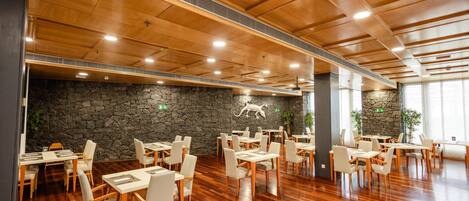 A spacious dining area with wooden flooring, stone walls, and multiple tables and chairs.