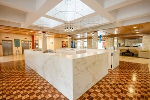 Un moderno vestíbulo de hotel con una recepción de mármol, piso de madera y un diseño geométrico en el techo.