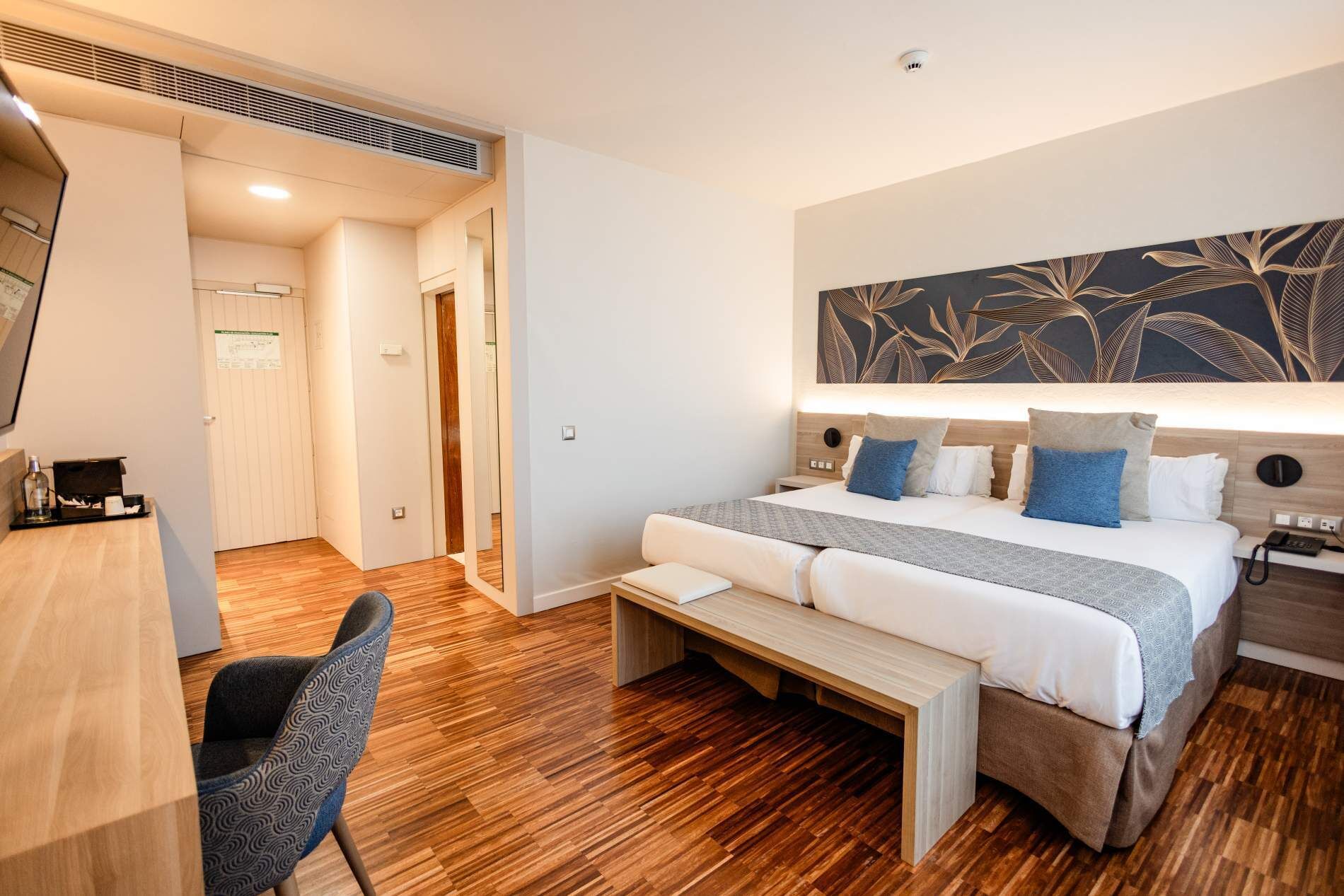 Una habitación de hotel con cama, mesita de noche, silla y una obra de arte grande en la pared.
