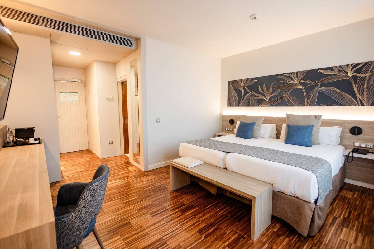Una habitación de hotel con cama, mesita de noche, silla y una obra de arte grande en la pared.