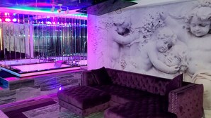 Una habitación con pared de diseño de mármol, un ventanal con persianas verticales, un sofá morado tapizado y un suelo con diseño de mármol.