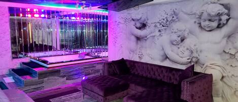 A room with a marble-patterned wall, a large window with vertical blinds, a purple tufted sofa, and a marble-patterned floor.