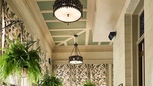 A sunlit hallway with patterned wallpaper, wicker furniture, and hanging plants.