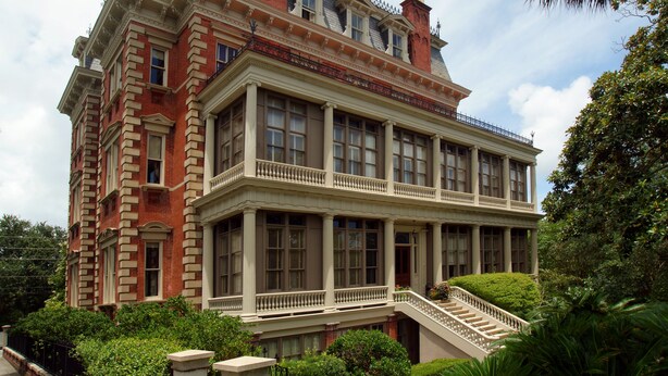 A large, historic building with multiple stories, featuring a prominent balcony and a grand staircase leading to the entrance.