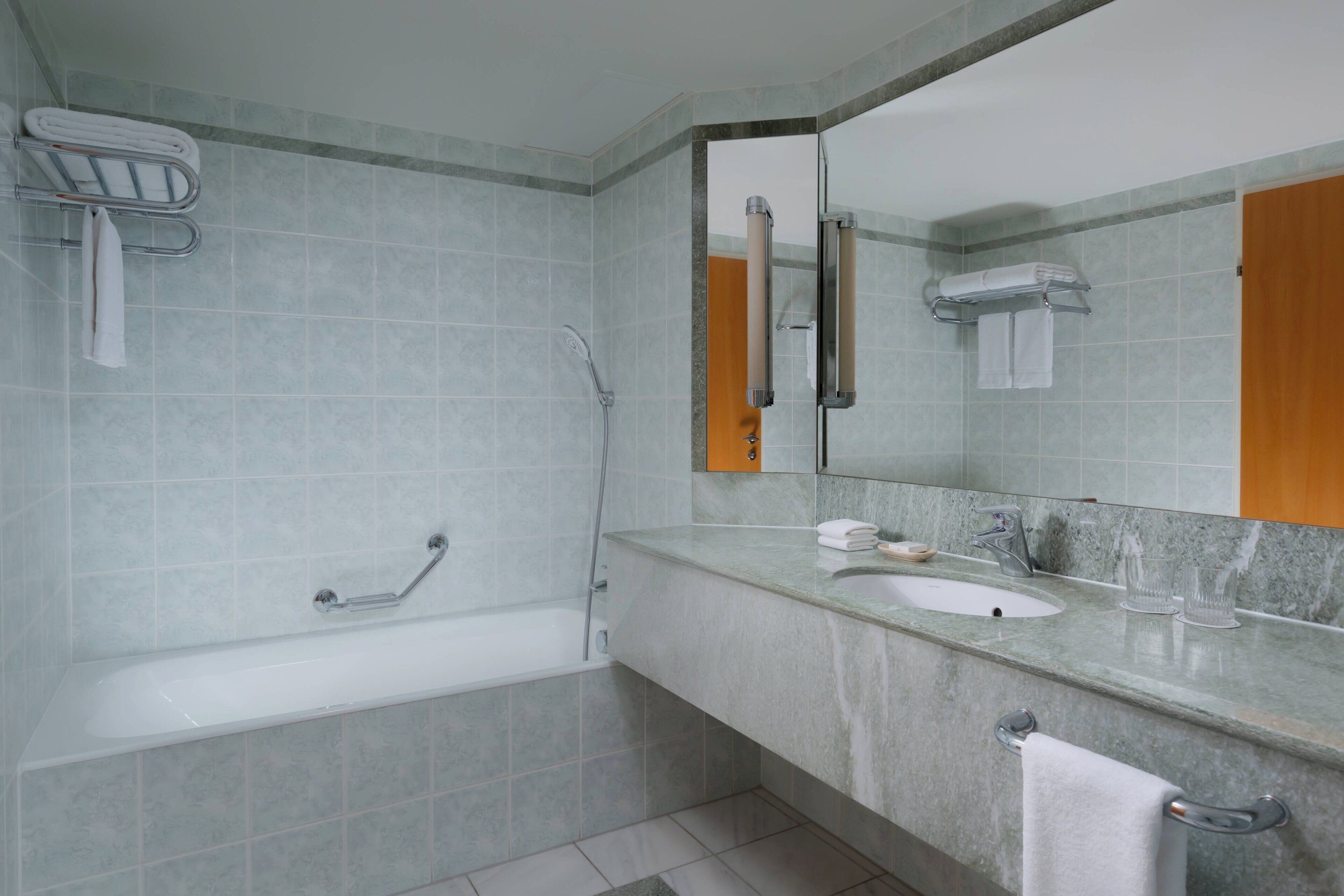 Un baño con bañera, lavamanos, espejo y toallero.