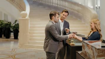 A reception area with a marble floor, a grand staircase in the background, and a chandelier.