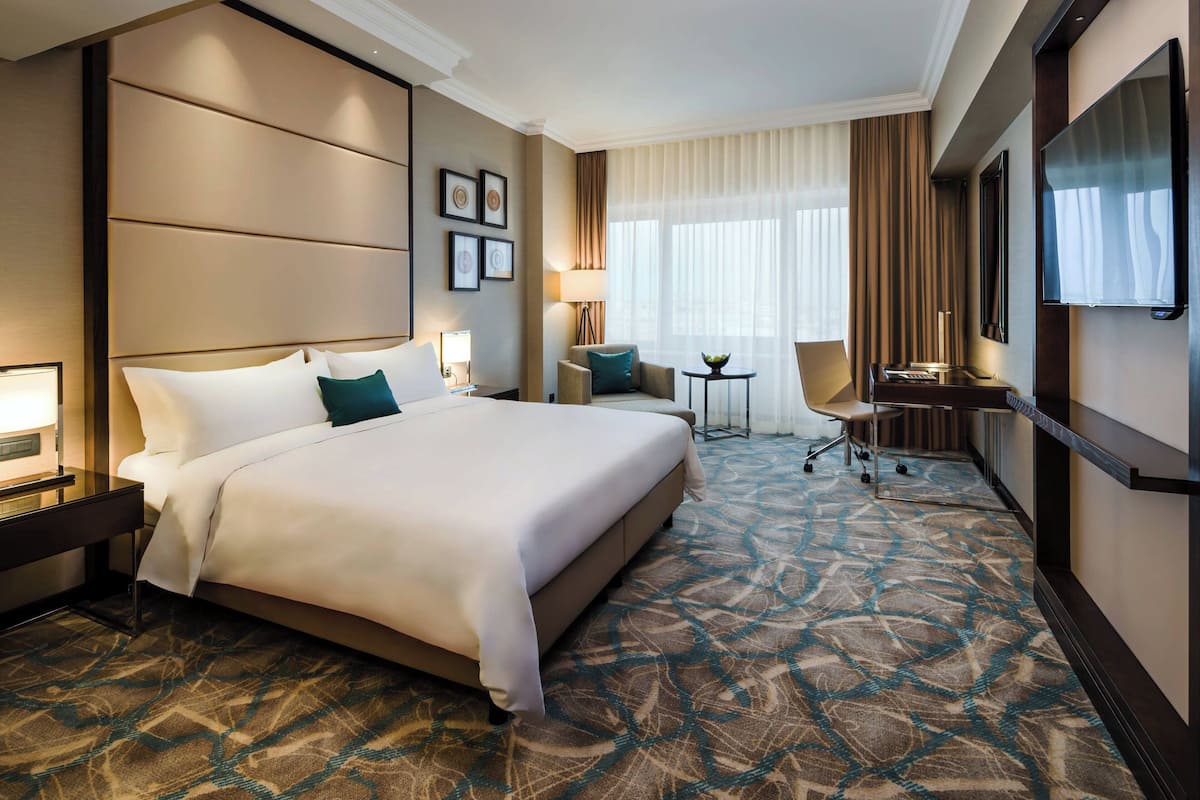 A hotel room with a large bed, a desk, a chair, a TV, and a patterned carpet.