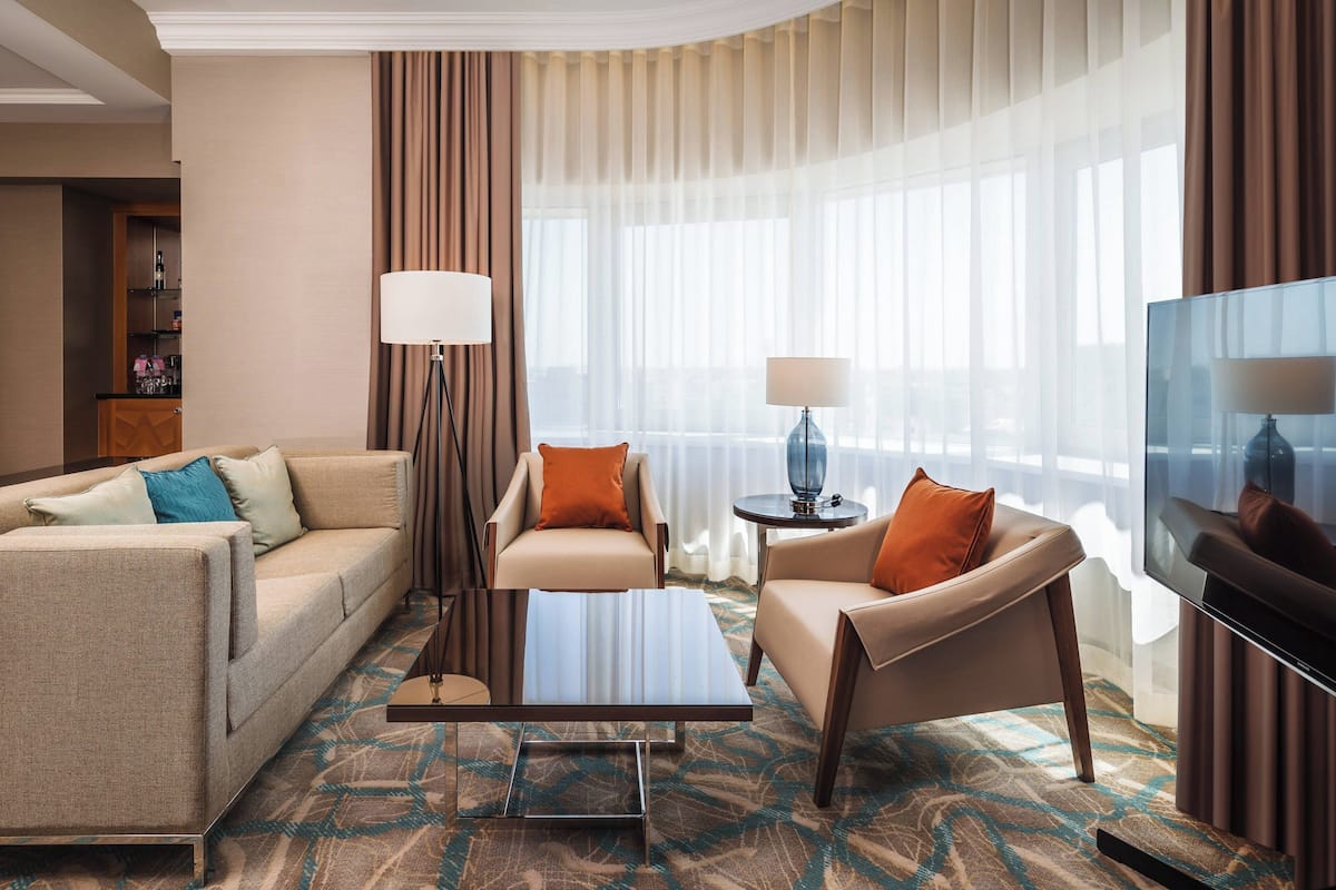 A hotel room with a sofa, two armchairs, a coffee table, a TV, and a lamp.