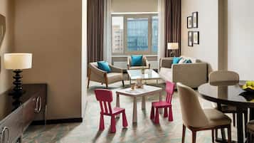 A hotel room with a seating area, a dining table, and a view of the cityscape.