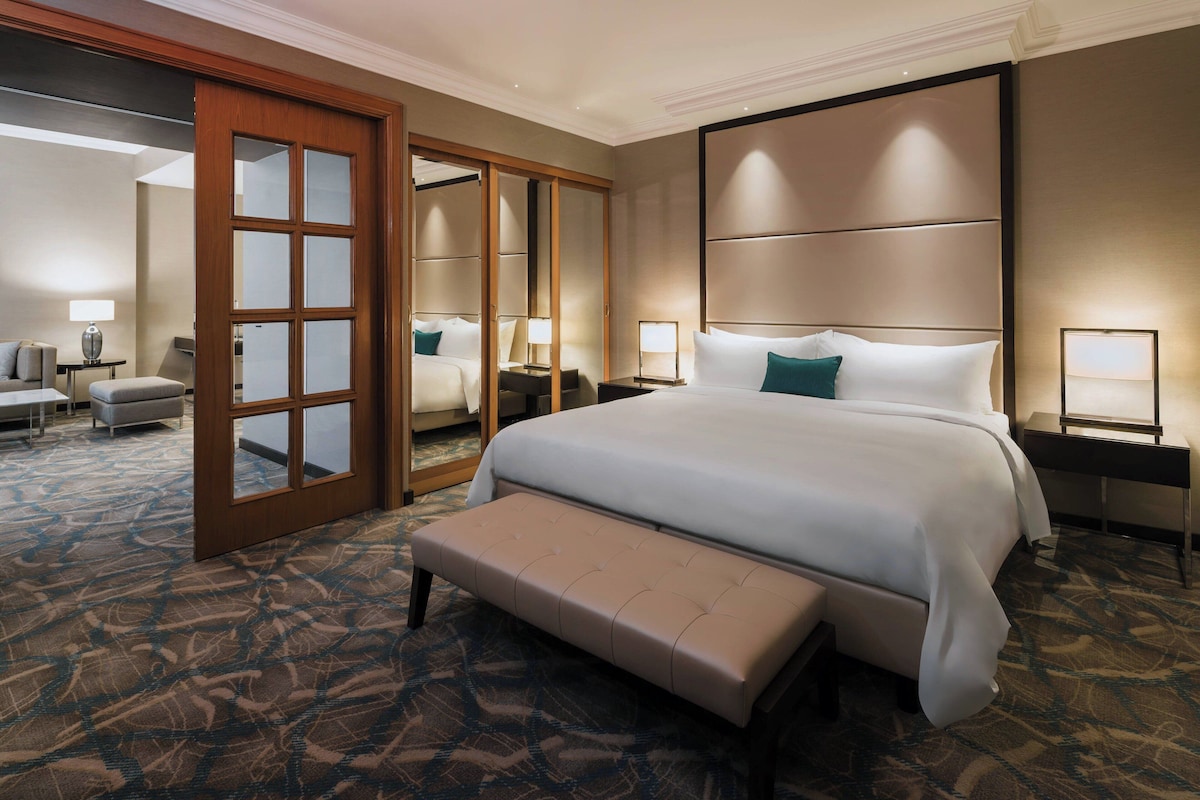 A hotel room with a large bed, a bench, a desk, and a chair.
