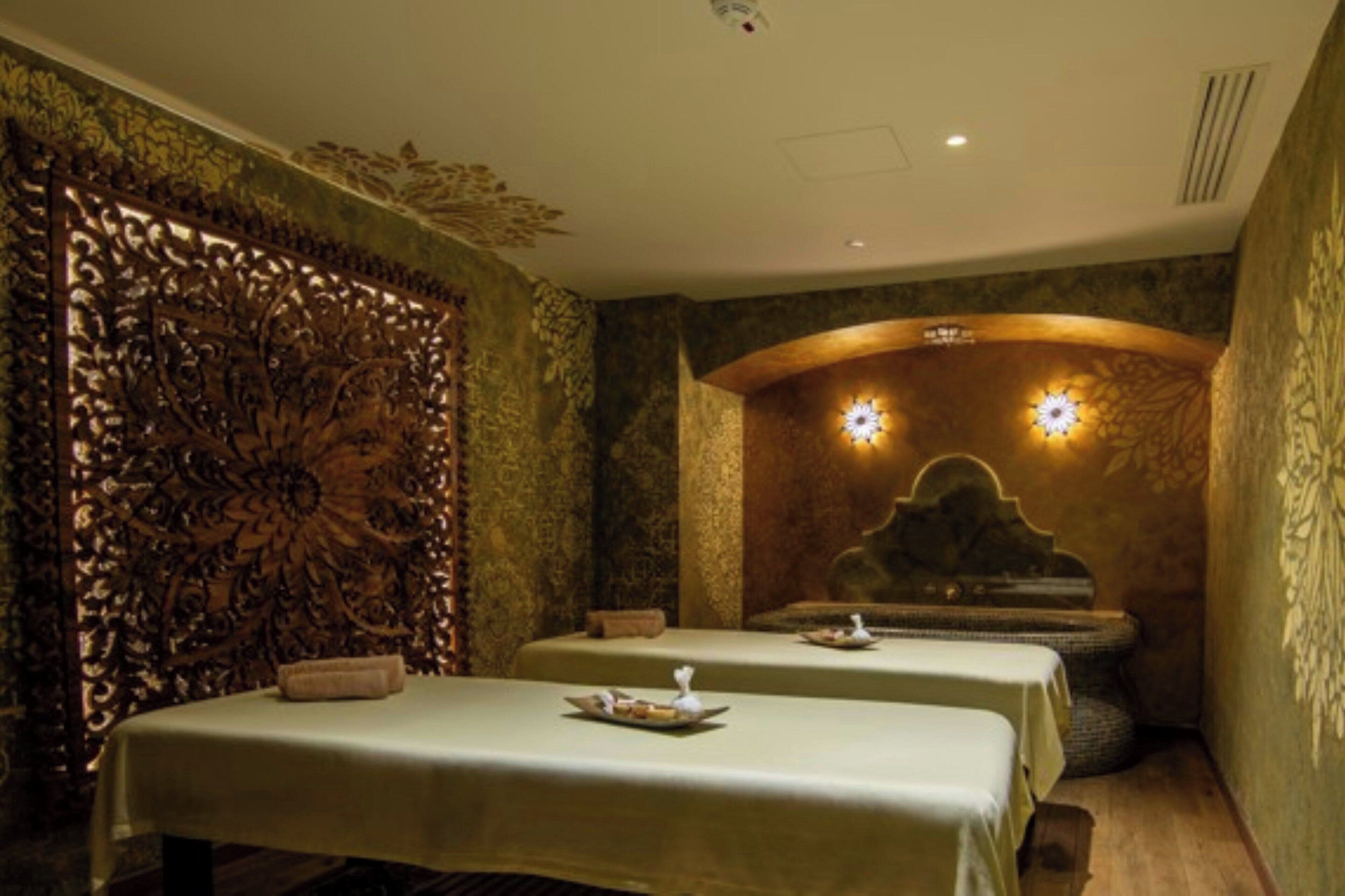 A spa room with two beds, ornate wall panels, and wall-mounted lighting.