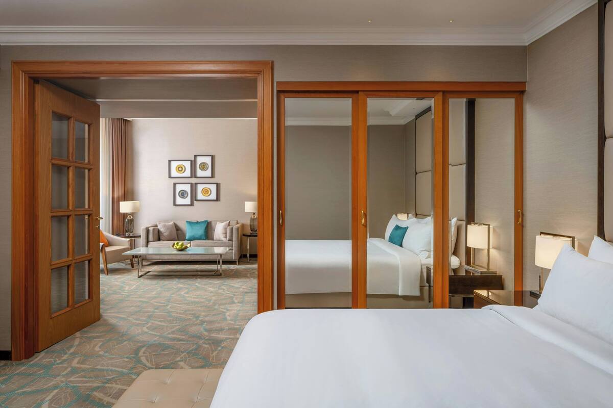 A hotel room with a large bed, a sofa, a desk, and a chair. There are framed pictures on the wall and a mirror on the door.