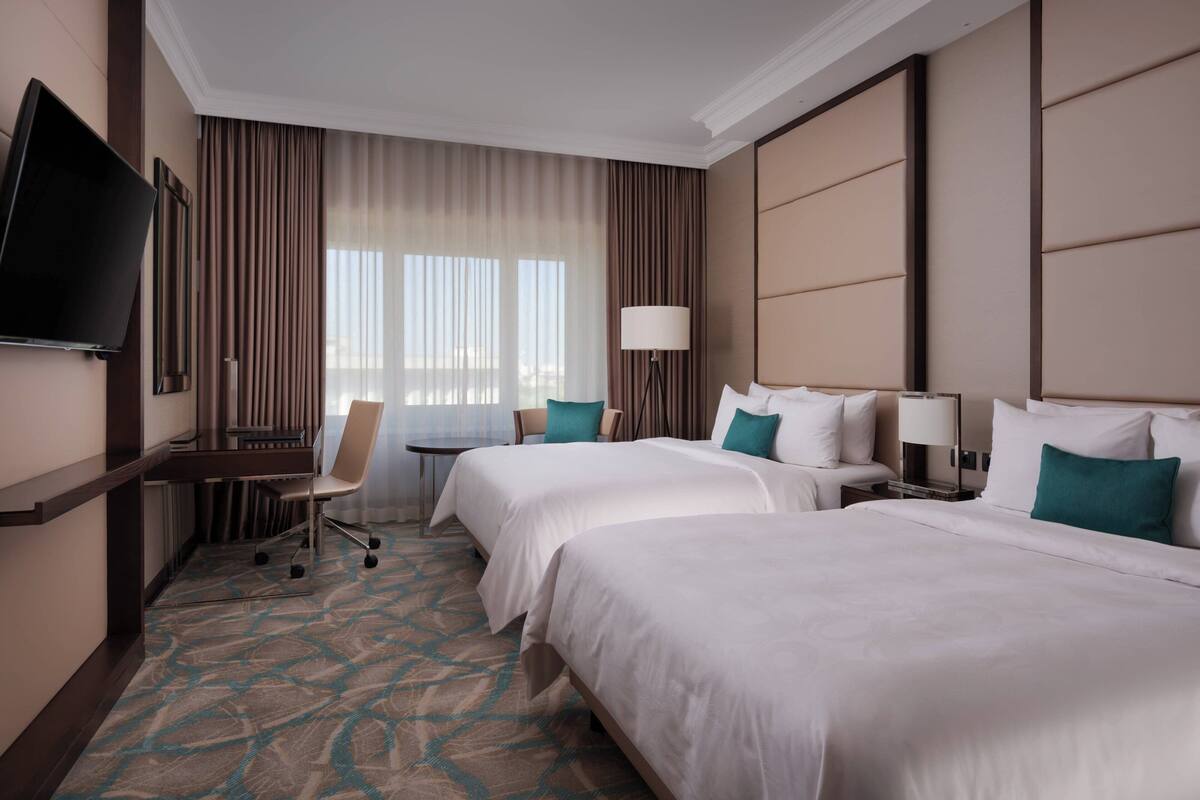 A hotel room with two beds, a desk, a chair, a TV, and a window with curtains.
