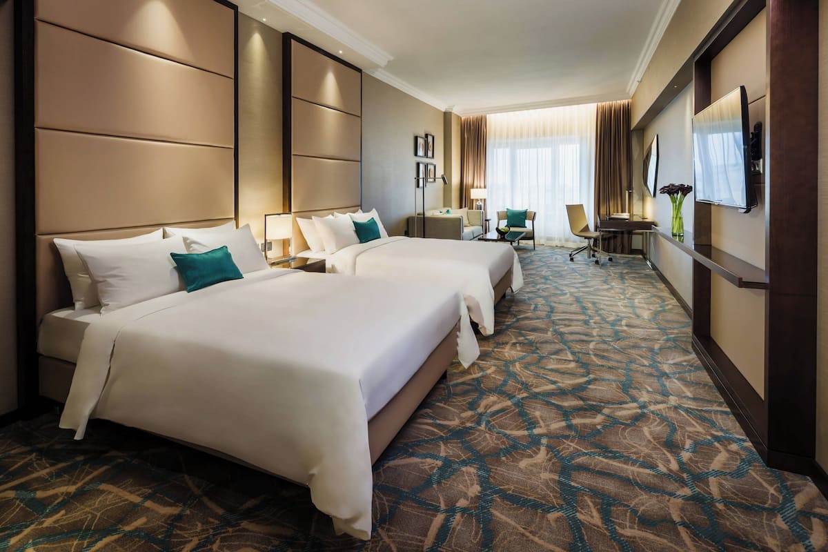 A hotel room with two beds, a desk, a chair, a TV, and a patterned carpet.