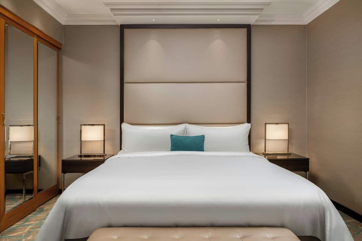 A hotel room with a large bed, two bedside tables with lamps, a mirror, and a wardrobe.