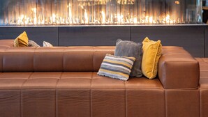 A modern living room with a leather sofa, circular ceiling lights, and a glass wall with a fire feature. - Marriott Indianapolis Downtown (Indianapolis)