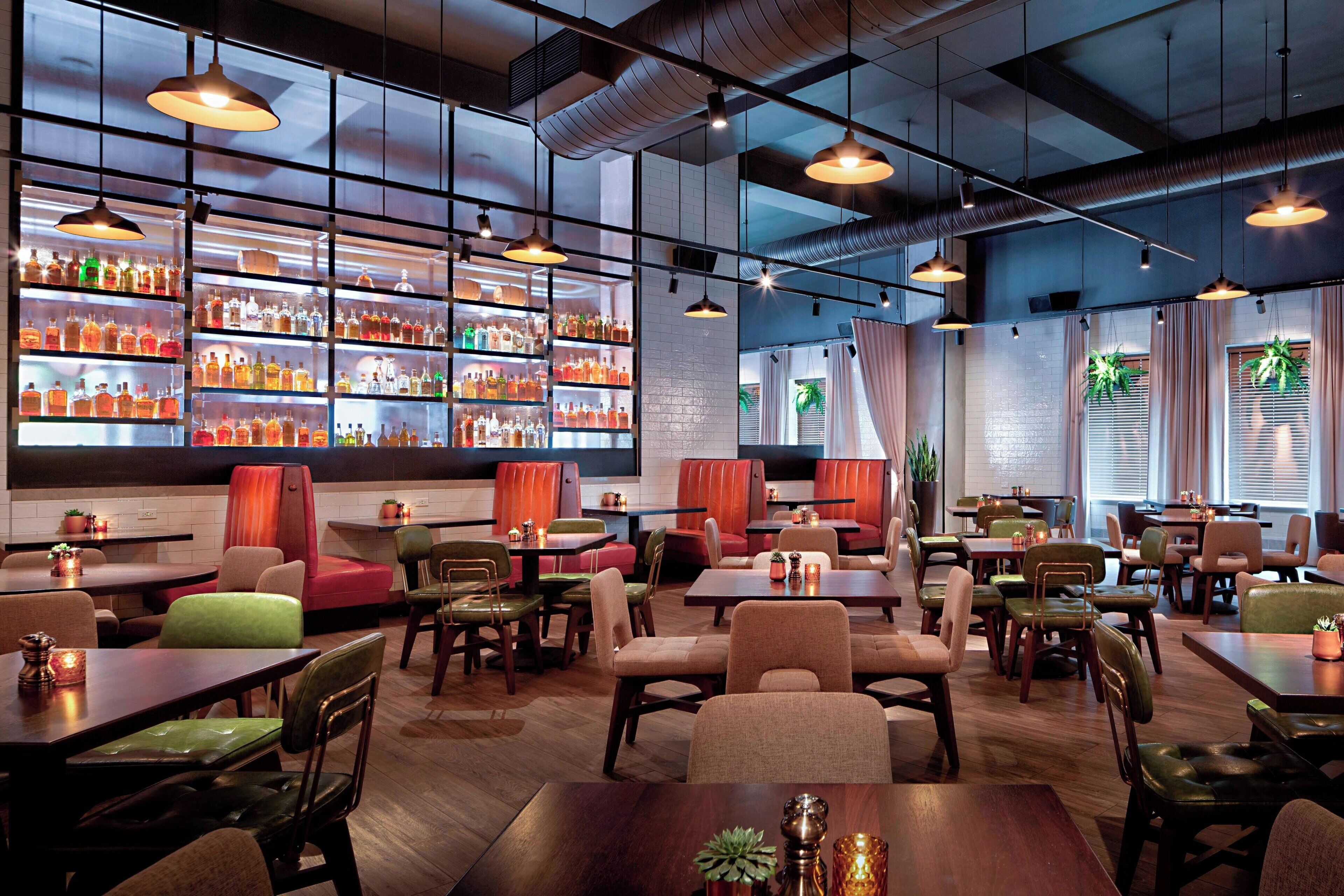 A modern restaurant with multiple seating areas, including booths and tables, and a bar area with shelves of bottles.