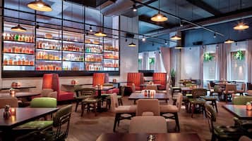 Un restaurante moderno con varias zonas de estar, incluyendo cabinas y mesas, y una zona de bar con estanterías llenas de botellas.