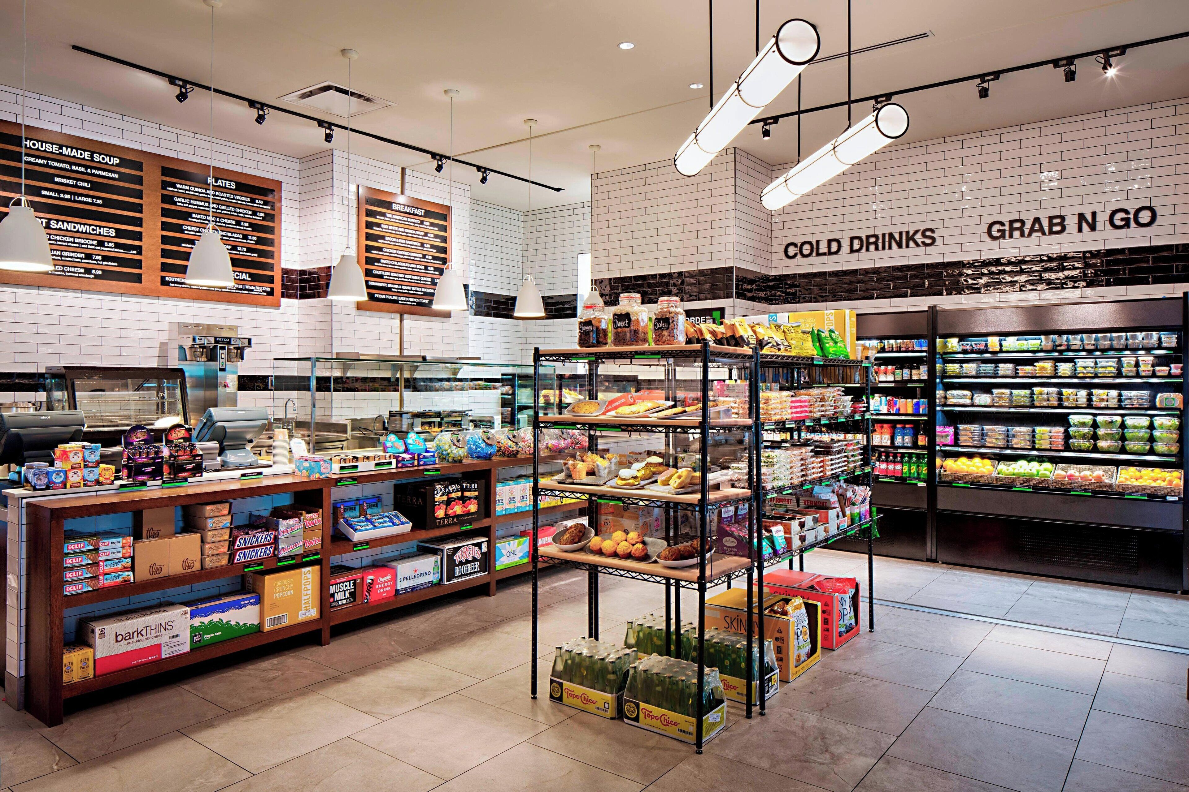 A grocery store interior with shelves stocked with various food items, a deli counter, and a section labeled 'COLD DRINKS'.