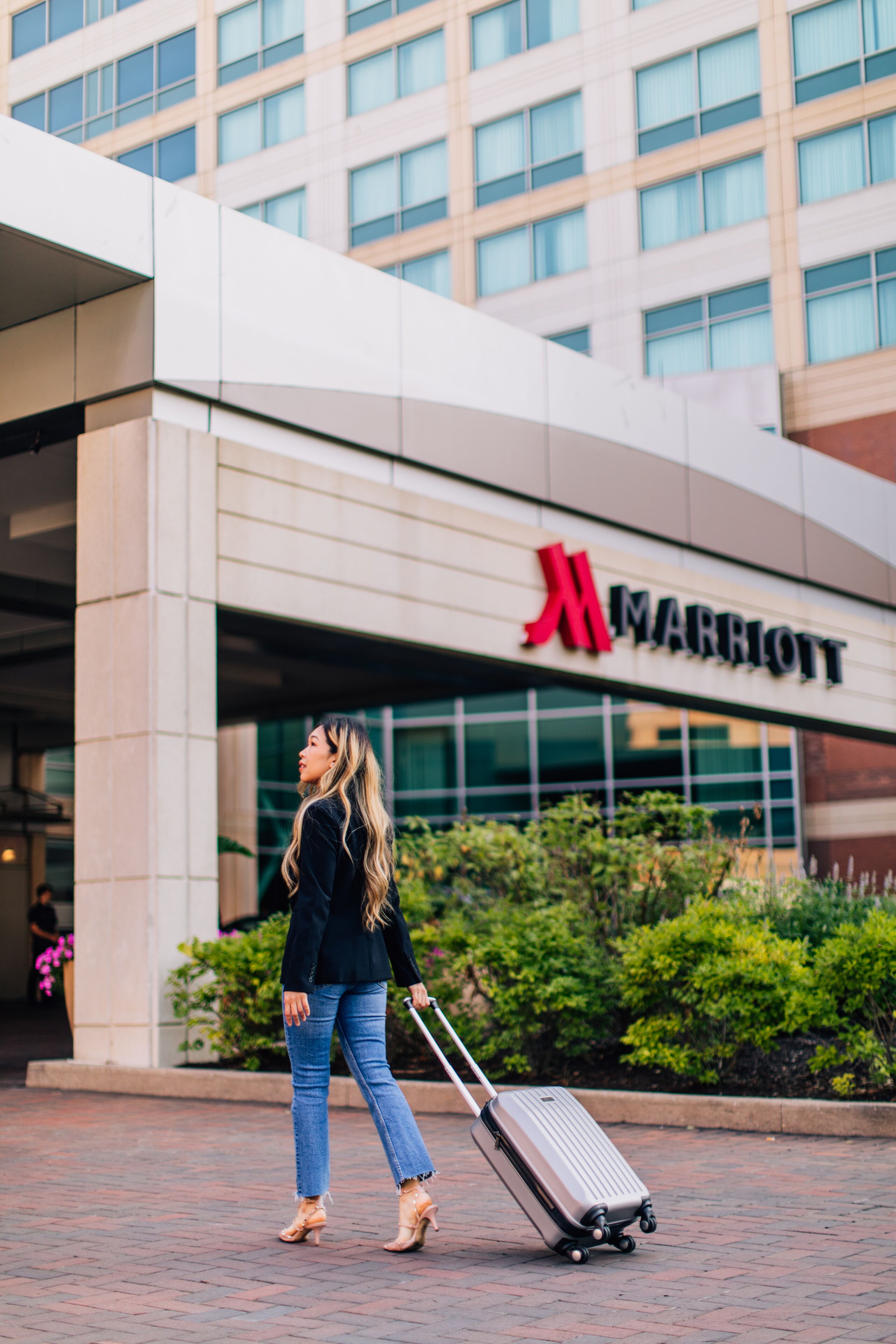 A woman walking towards a Marriott hotel entrance with a suitcase.