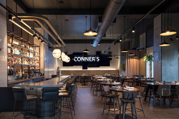 A modern bar area with a long counter, bar stools, and a neon sign reading "CONNER'S".