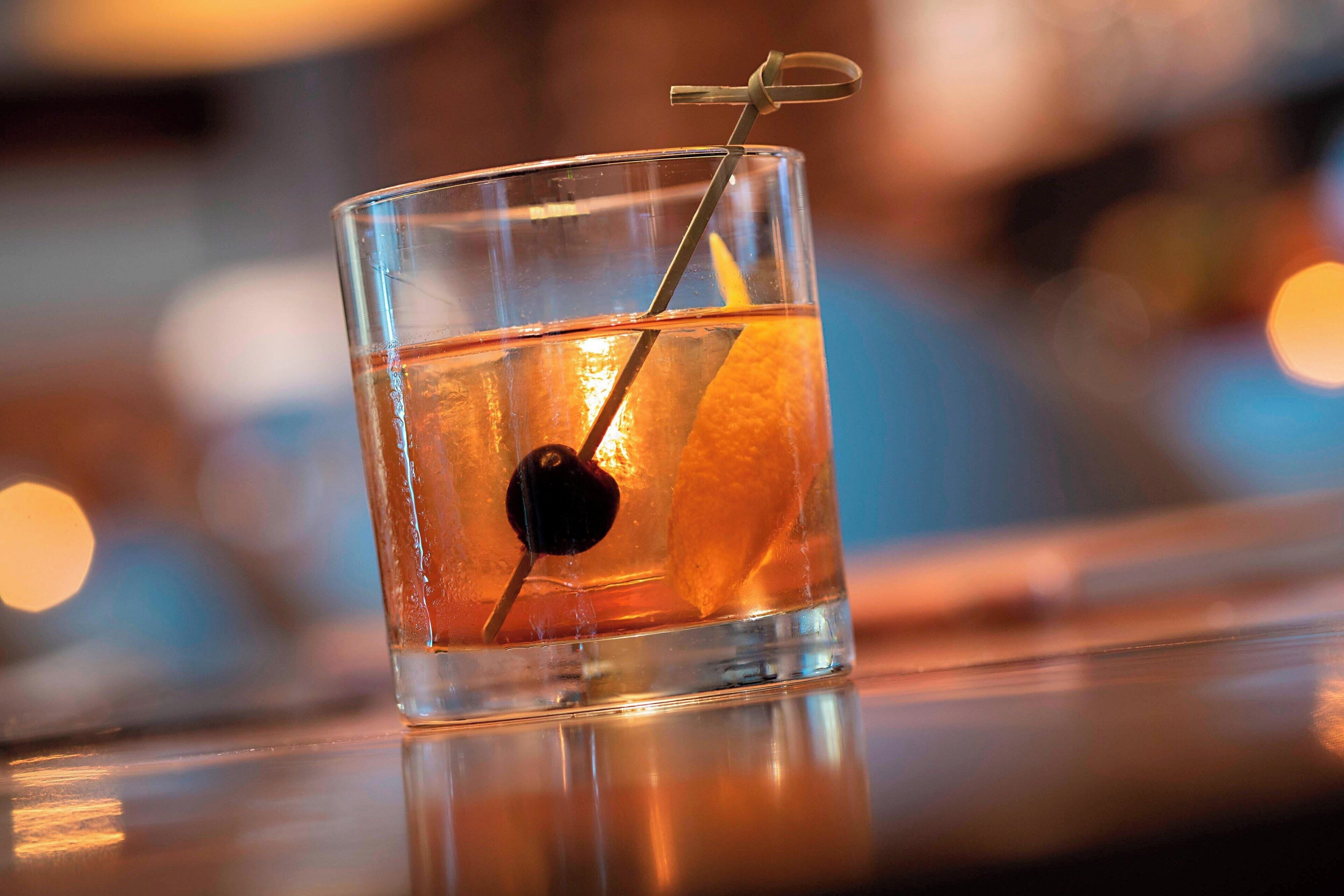 A clear glass with a lemon slice and a cherry, placed on a reflective surface.