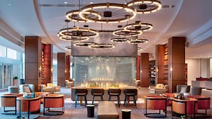 A modern lobby with circular ceiling lights, seating areas, and a large glass wall with a view of the city. - Marriott Indianapolis Downtown (Indianapolis)