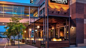 A modern building with a restaurant named "CONNER'S KITCHEN+BAR" featuring outdoor seating with fire pits. - Marriott Indianapolis Downtown (Indianapolis)