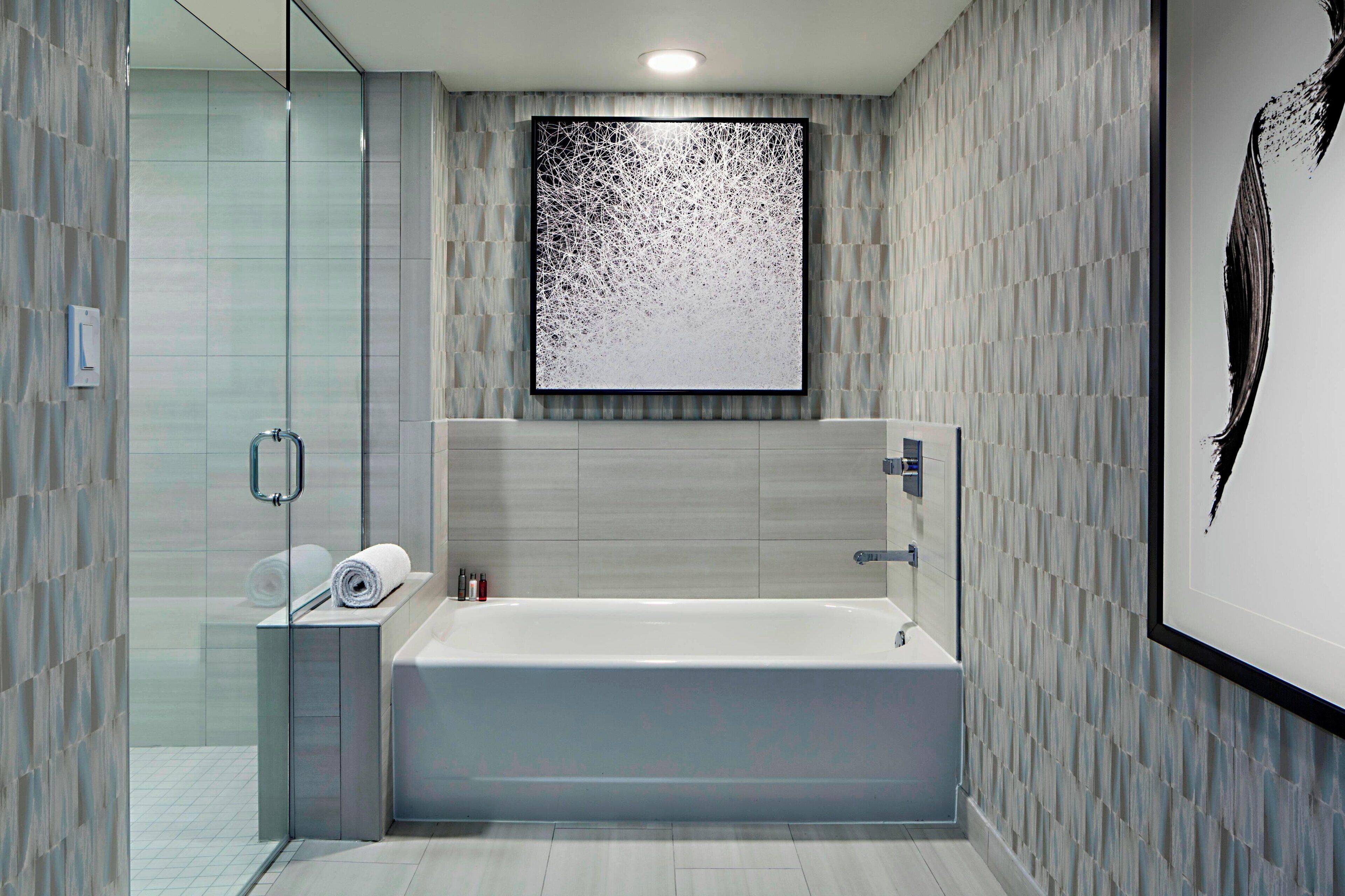 A modern bathroom with a freestanding bathtub, a glass shower enclosure, and a large abstract artwork on the wall.