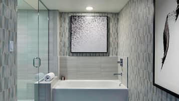 A modern bathroom with a freestanding bathtub, a glass shower enclosure, and a large abstract artwork on the wall.