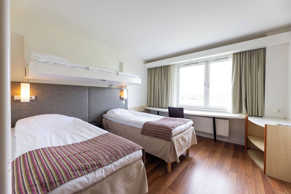 A hotel room with two beds, a desk, and a window with curtains.