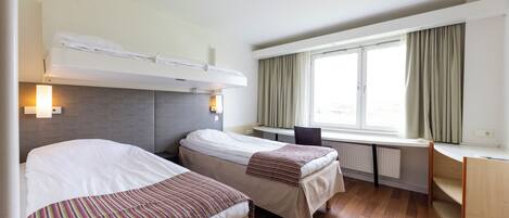 A hotel room with two beds, a desk, and a window with curtains.