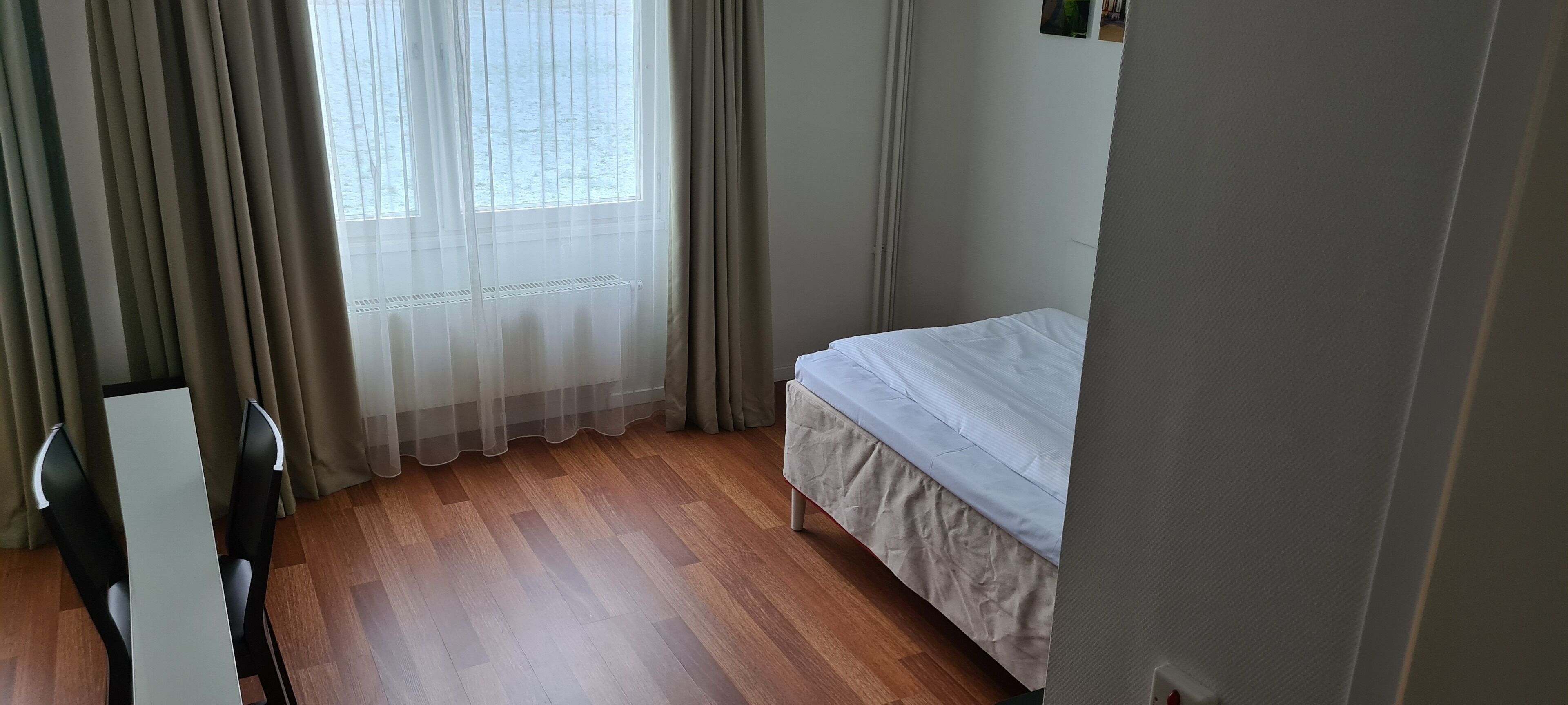 A room with a bed, a chair, a table, and a window with curtains.