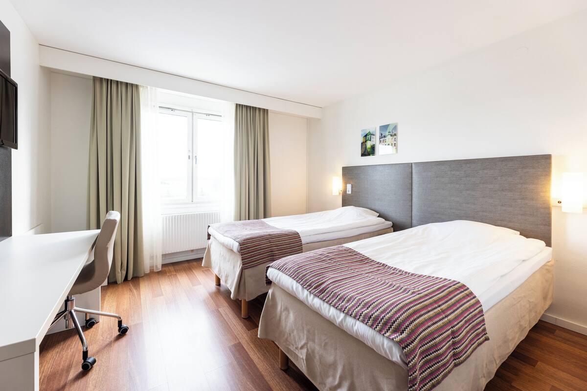 A hotel room with two single beds, a desk, and a chair.