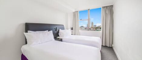 Habitación de hotel con dos camas, una ventana con cortinas y vista a la ciudad.