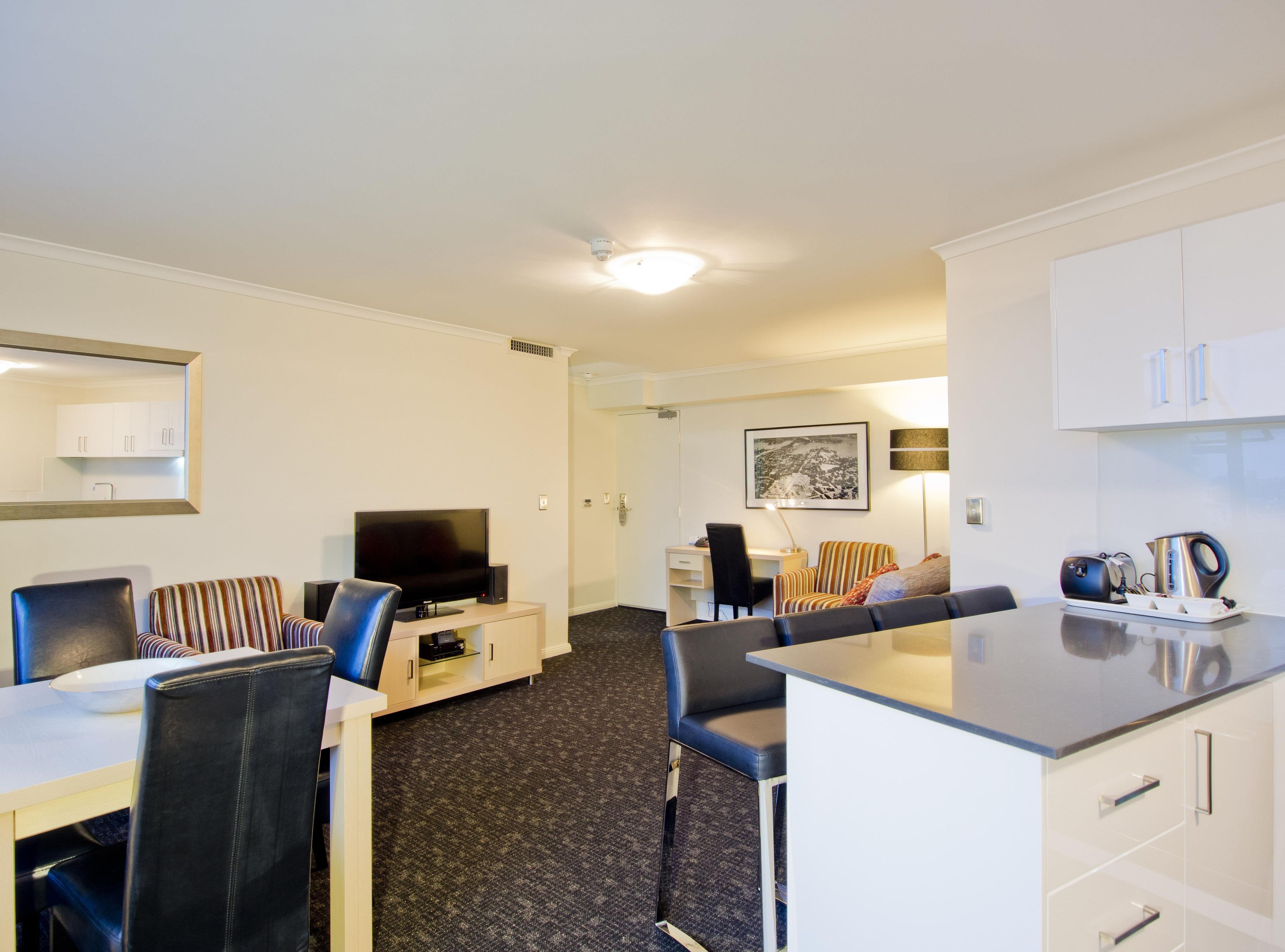 A modern hotel room with a dining area, a television, a coffee maker, and a framed picture on the wall.