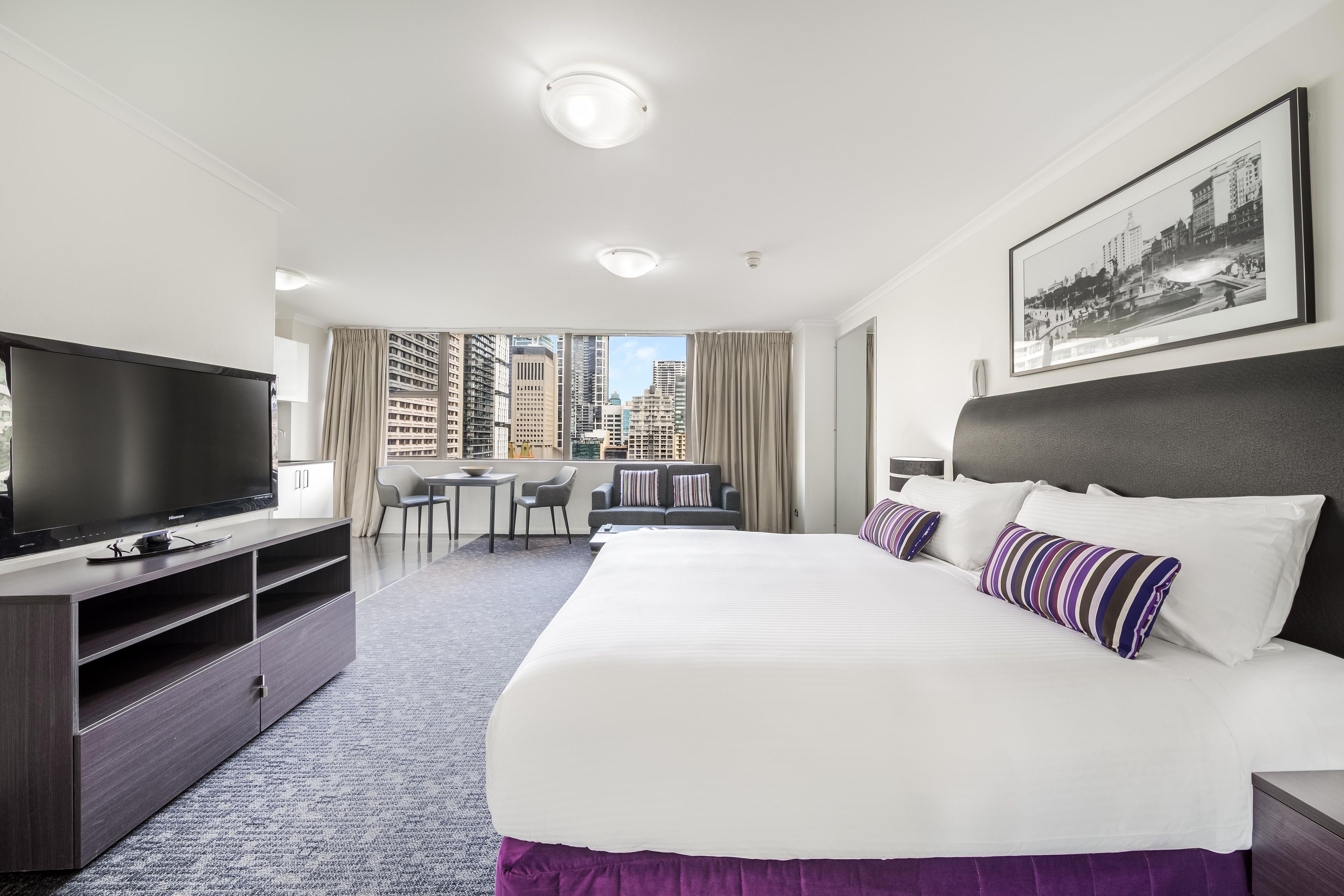 A hotel room with a bed, television, desk, and city view.