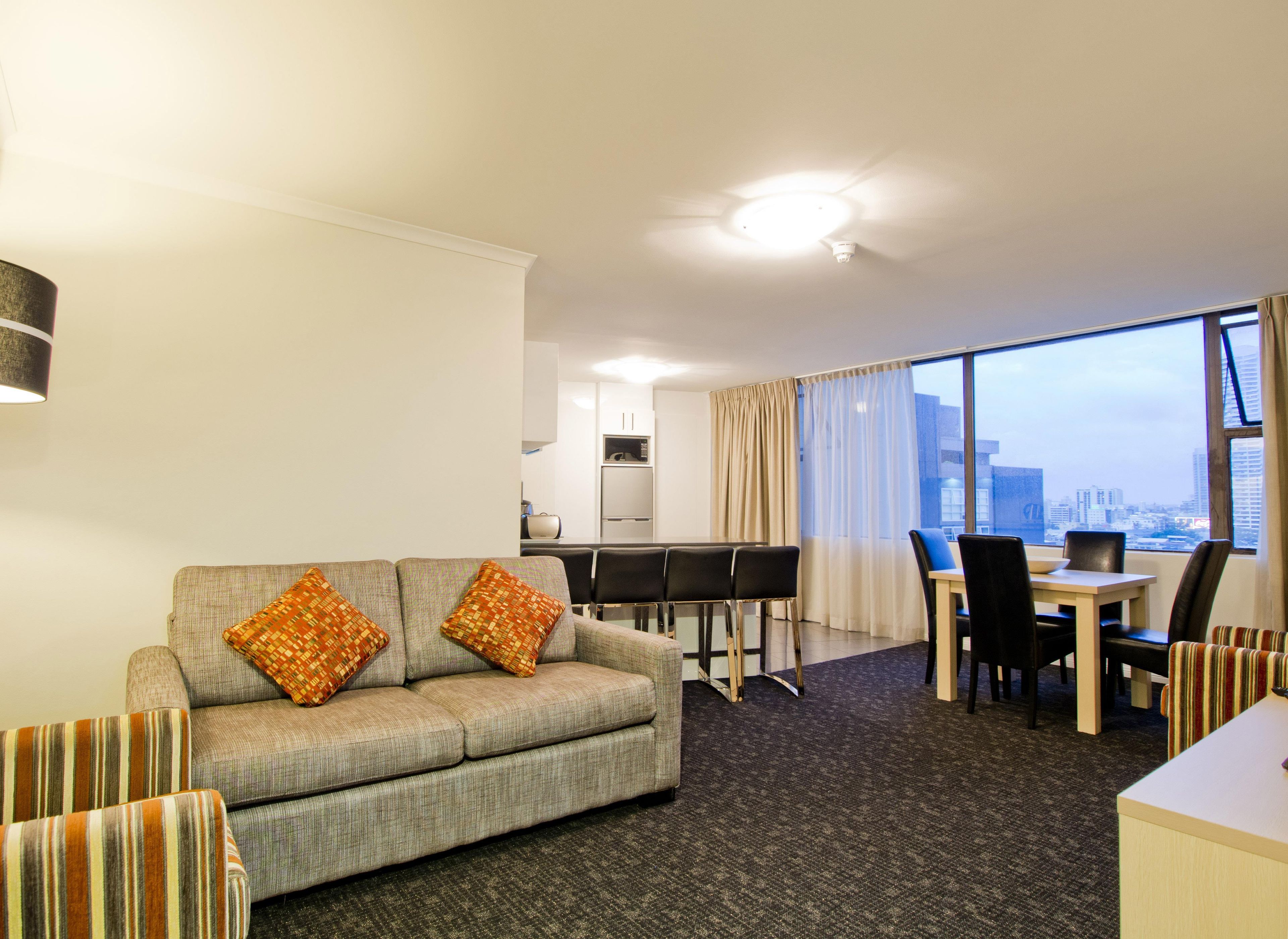 A hotel room with a sofa, dining table, chairs, and a view of the city.