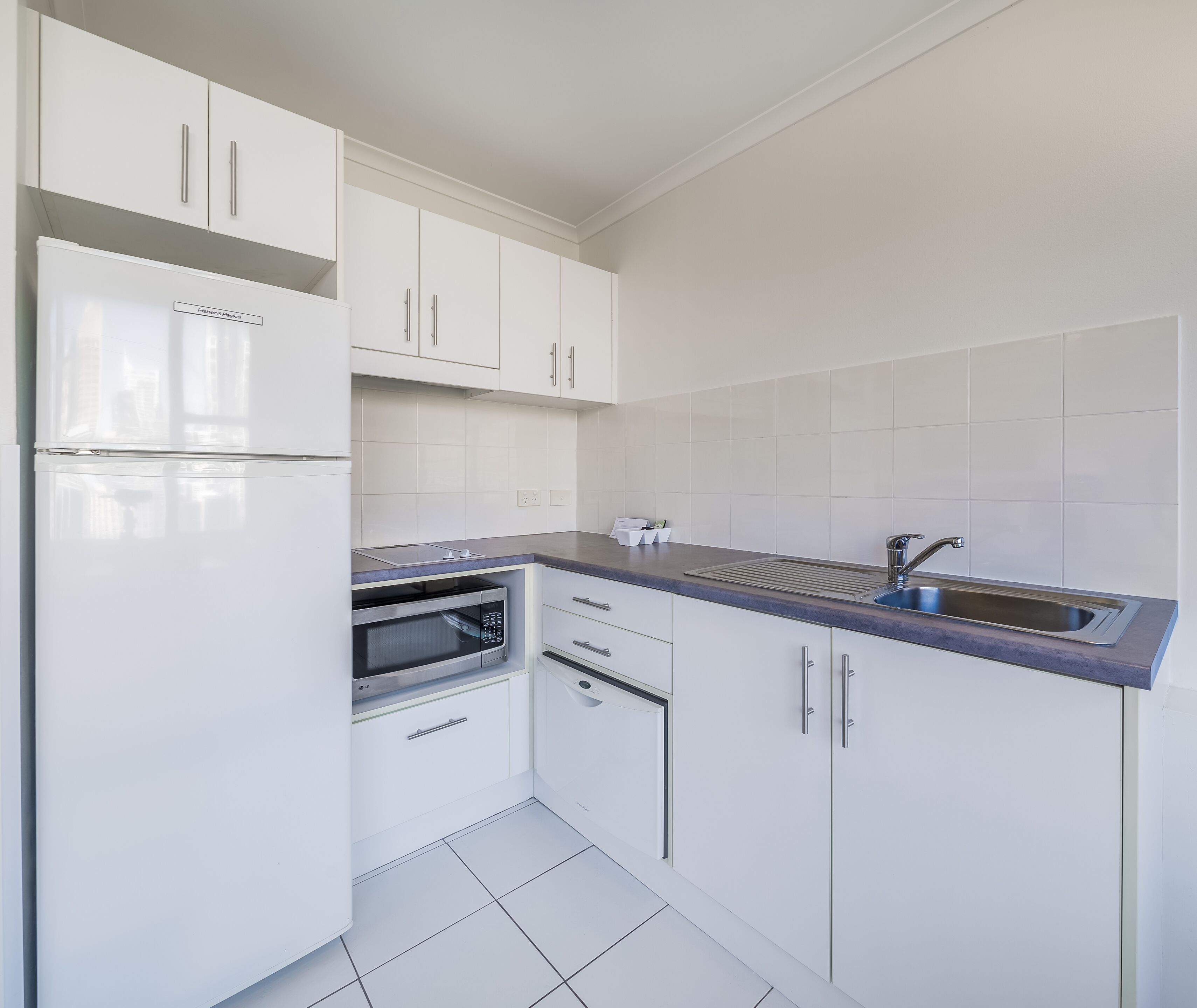 A modern kitchen with white cabinets, a built-in microwave, and a stainless steel sink.