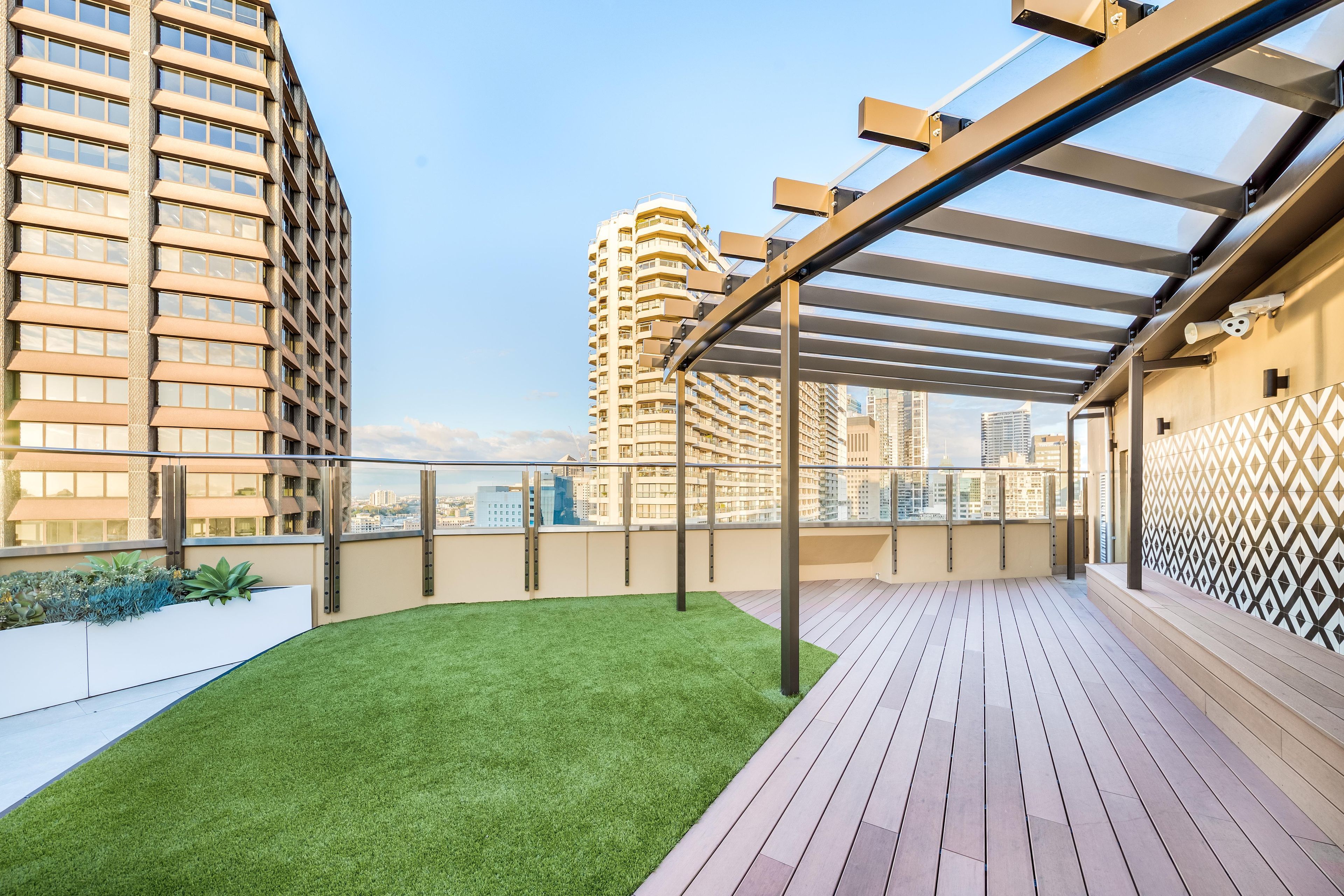 Eine Dachterrasse mit Holzdeck, künstlichem Rasen und Blick auf die umliegenden Hochhäuser.