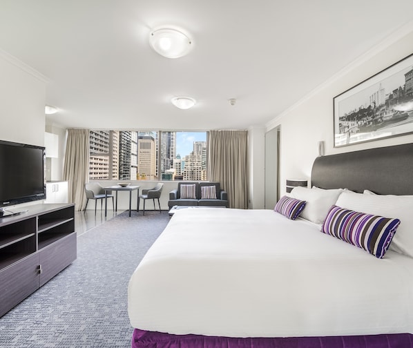 Een hotelkamer met een groot bed, een televisie, een bureau en uitzicht op hoge gebouwen.