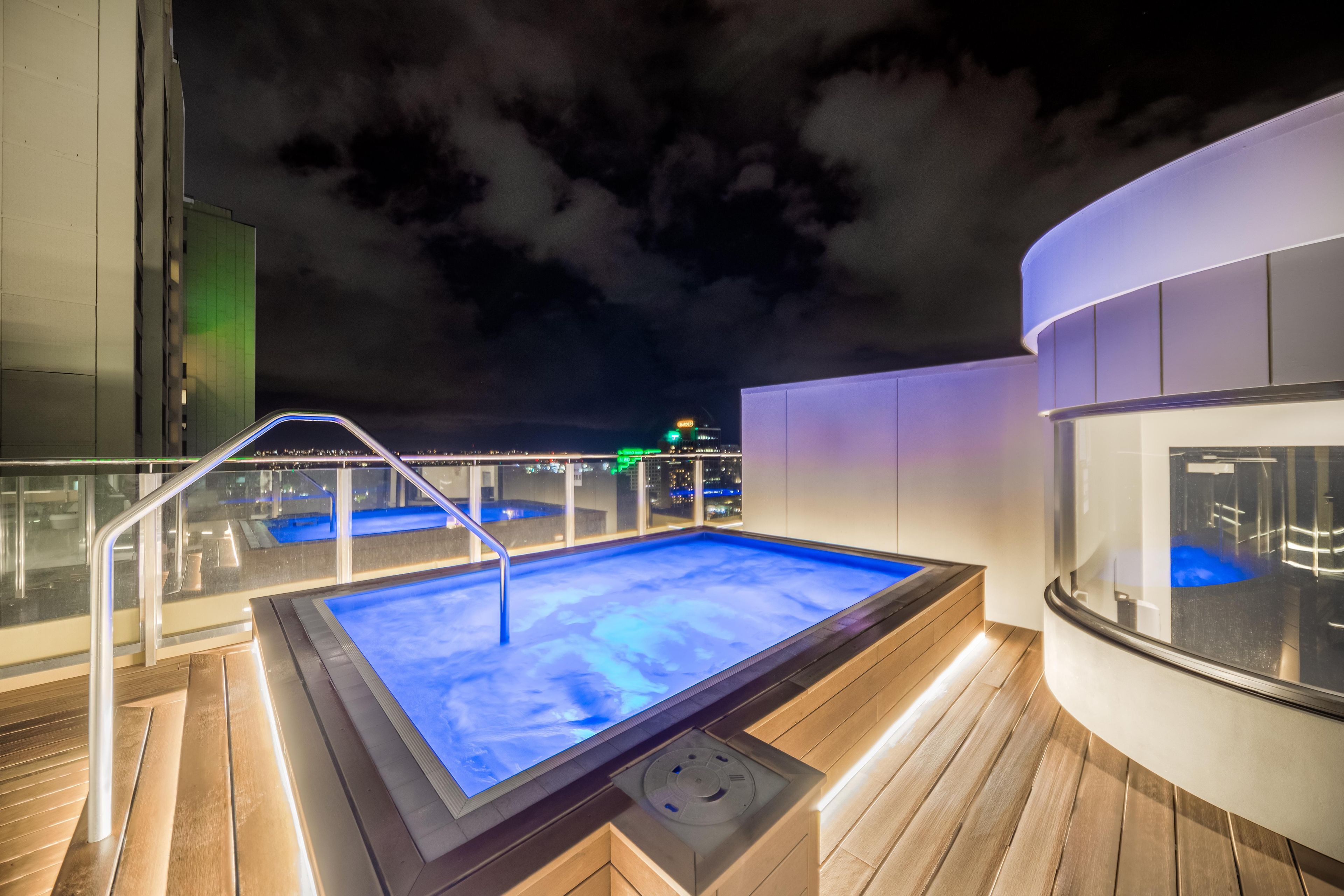 A heated outdoor pool area with a glass barrier and a wooden deck.